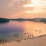 Vue aérienne du lac de Sanguinet au coucher du soleil avec des personnes se baignant et faisant du paddle.