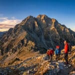 Groupe de randonneurs admirant le massif du Canigou au lever du soleil sur un sentier escarpé.
