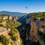 Vue panoramique des gorges de la Nesque avec une route sinueuse, un cycliste, une chapelle troglodyte et le mont Ventoux.