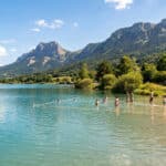 Baigneurs dans les eaux turquoise du lac Marandan avec les montagnes et une tente en arrière-plan sous un ciel bleu.