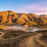 Montagnes colorées de rhyolite et sources chaudes fumantes dans un paysage islandais sous une lumière dorée.