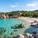 Une crique aux eaux turquoise cristallines bordée de rochers granitiques et de maquis méditerranéen en Sardaigne.