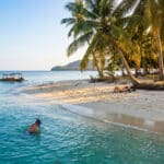 Plage de sable blanc à Gili Trawangan avec une personne faisant du snorkeling et un bateau traditionnel au loin.